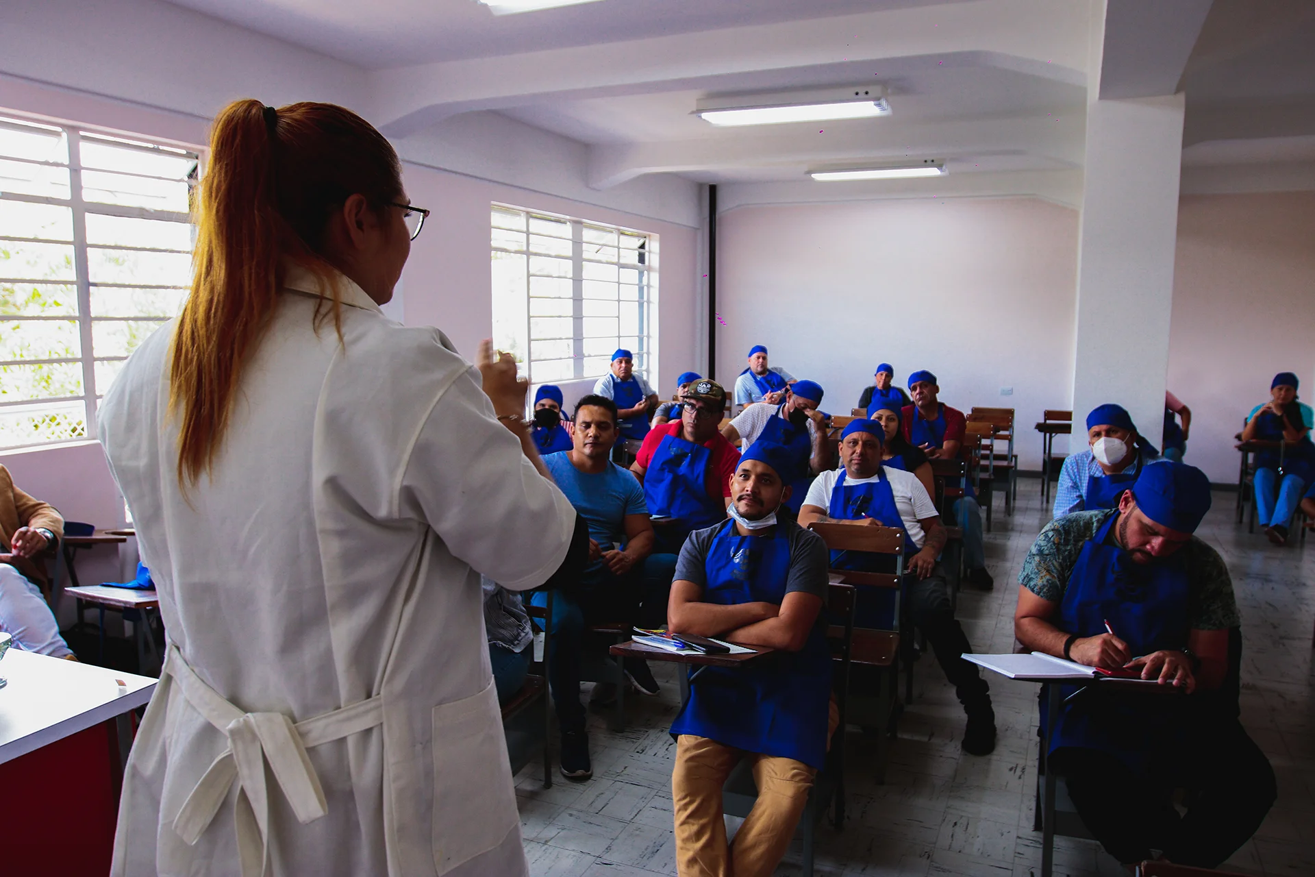 Norka Rojas dando una clase teórica a un grupo de estudiantes sentados en un aula