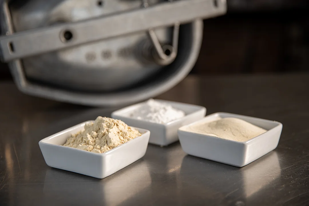 Tres cuencos con distintos polvos de curado —claro, blanco y beige— junto a una balanza industrial