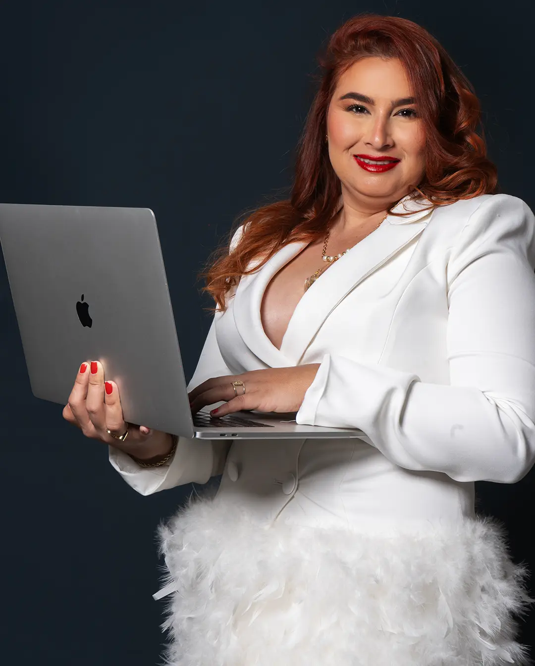Norka Rojas, Maestra Charcutera, posando con una laptop, con blazer blanco sobre fondo azul oscuro
